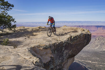 Man with umbrella on rock against sky