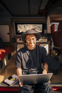 Happy young man using laptop while sitting in van during vacation