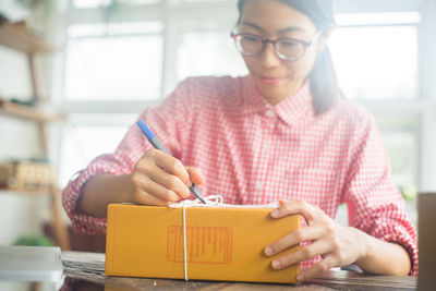 Young woman writing on cardboard box at home