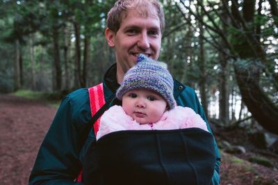 Portrait of smiling father carrying daughter in forest