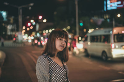 Portrait of young woman standing on illuminated street at night