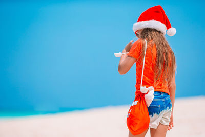 Woman holding umbrella standing at beach against blue sky