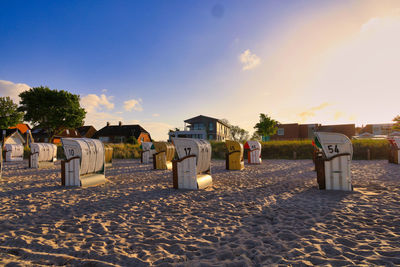 Hooded chairs on beach against sky during sunset