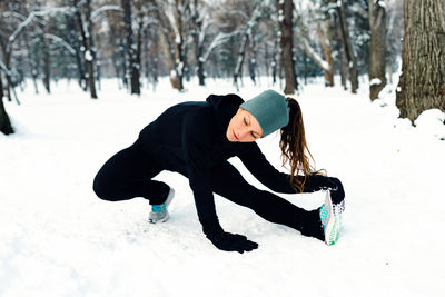 Woman exercising on snowy field against bare trees