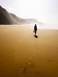 Rear view of man walking on beach against sky