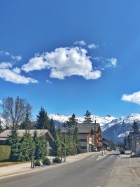 Road by buildings against blue sky