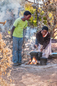 Woman with son preparing food on campfire outdoors