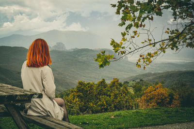 Woman sitting on picnic table against mountains