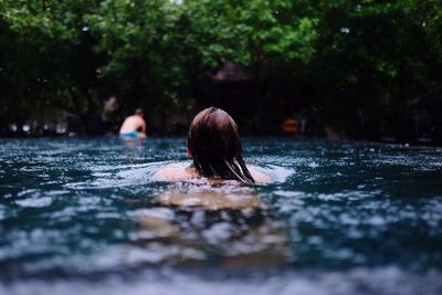 Rear view of woman swimming in lake at forest