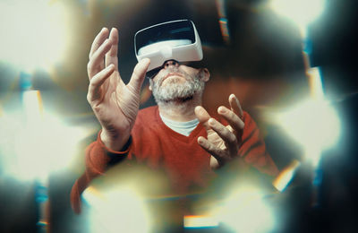 Low angle view of senior man using virtual reality headset amidst illuminated lights