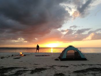 People standing on beach against sky during sunset