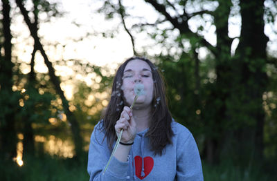 Teenage girl blowing bubbles standing against trees