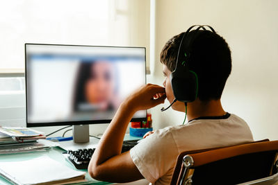 Rear view of boy using computer while sitting at table