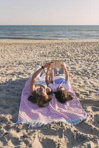 Young female friends reading book while lying on picnic blanket at beach