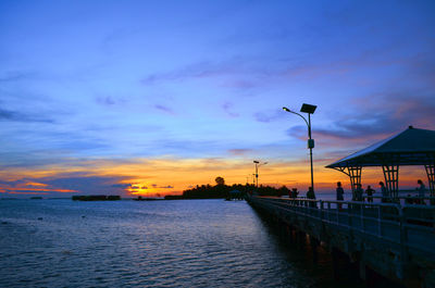 Street by sea against sky at sunset