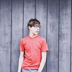Teenage boy standing against wooden wall