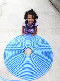 High angle view of smiling girl sitting by garden hose on footpath