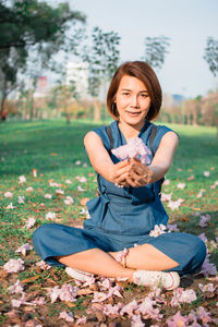 Portrait of woman holding flowers while sitting on field at park