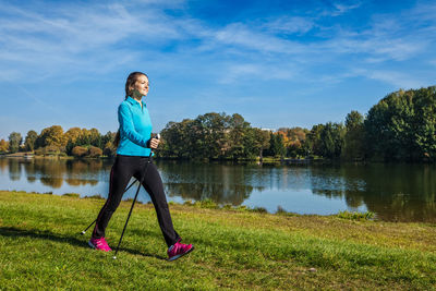 Side view of woman exercising on lake against sky