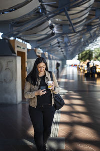 Smiling woman using cell phone while walking at train station