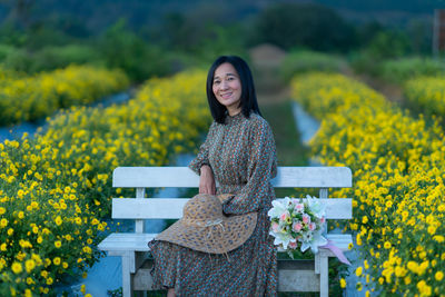 Portrait of a smiling young woman standing on yellow flowering plants