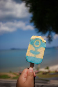 Close-up of hand holding ice cream cone against sky