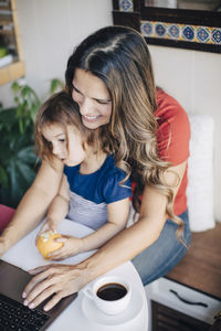 Mother working over laptop while daughter sitting on lap at table