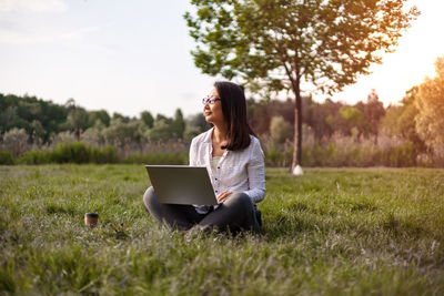 Woman using laptop while sitting on field