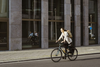 Businesswoman cycling on road near building in city