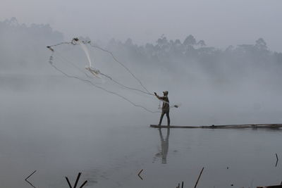 Man fishing in lake against sky