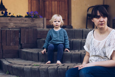 Thoughtful mother and daughter sitting on steps