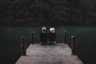 Rear view of couple sitting by lake on pier