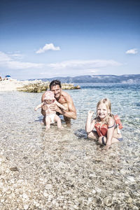 Portrait of happy family enjoying in sea against blue sky during sunny day