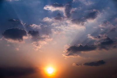 Low angle view of sunlight streaming through clouds during sunset