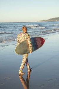 Man wearing suit carrying surfboard while walking at beach