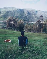 Rear view of man sitting on field against sky