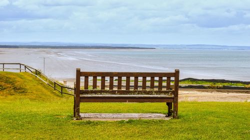 Empty bench on beach by sea against sky