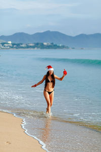 Portrait of young woman standing on beach against sky