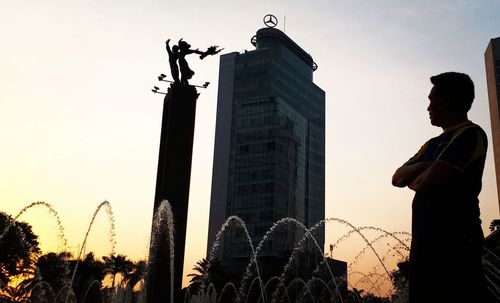 Low angle view of silhouette man standing by building against sky