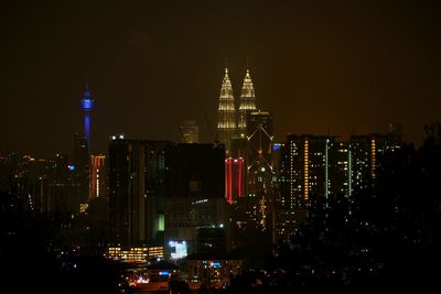 Petronas towers and menara kuala lumpur tower in illuminated city against sky at night