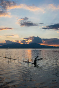 Silhouette people in lake against sky during sunset