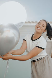 Young woman holding balloon standing against sky