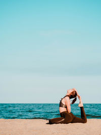 Side view of young woman doing yoga on beach against sky