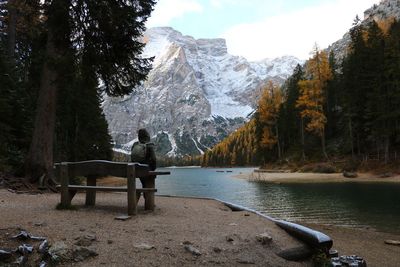 Rear view of man sitting on shore by lake against sky