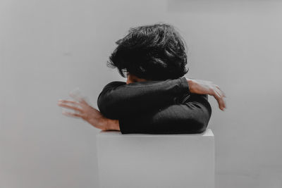 Rear view of man sitting against wall