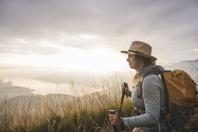 Woman with backpack and hiking poles standing under sky