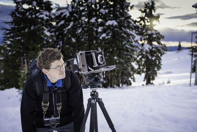 Mature man with backpack and tripod standing on snow