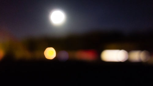 Defocused image of illuminated lights against sky at night