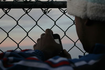 Close-up of hand on chainlink fence against sky