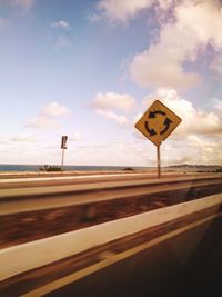 Road sign by sea against sky